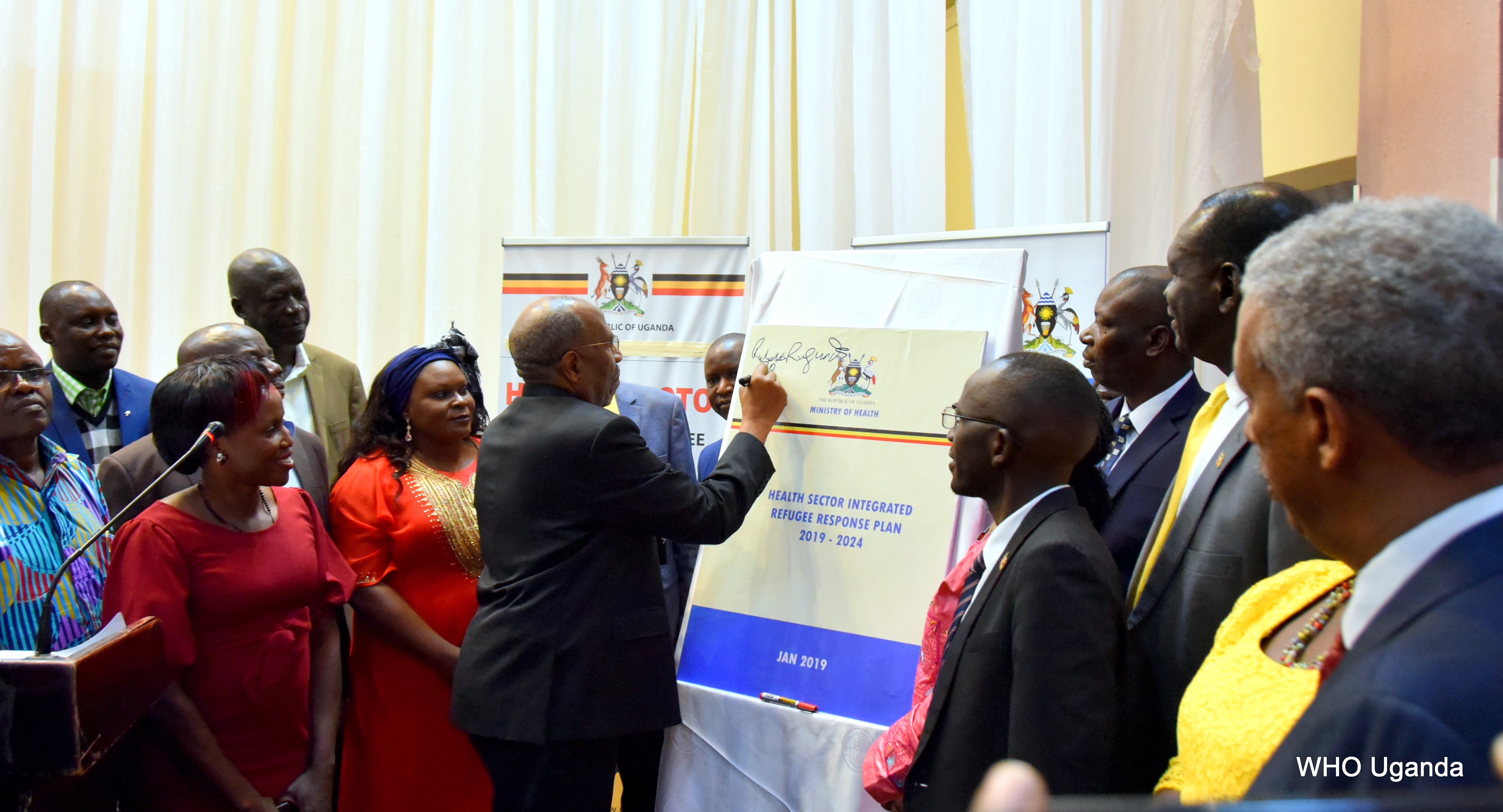 Prime Minister of Uganda Dr Ruhakana Ruganda signs on a dummy copy of the HSIRRP to launch the plan as government officials and partners look on 