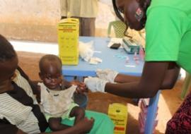 A laboratory technician draws blood from a child to test for malaria at an outreach post in Lologo Central Equatoria State, supported by WHO to mark World Malaria Day