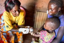 Pascaline, un relais communautaire, pique délicatement le doigt d’Elissa pour recueillir un peu de sang qui servira ensuite à déterminer à l’aide d’un test de diagnostic rapide si l’enfant est atteint de paludisme.