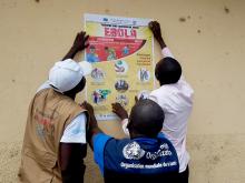 A Kasenye, en Ituri, les mobilsateurs sociaux du Ministère de la Santé et de l'OMS travaillent la main dans la main pour sensibiliser les communautés à l'aide des messages clés sur Ebola en plaçant les affiches dans le village - OMS/Eugene Kabambi