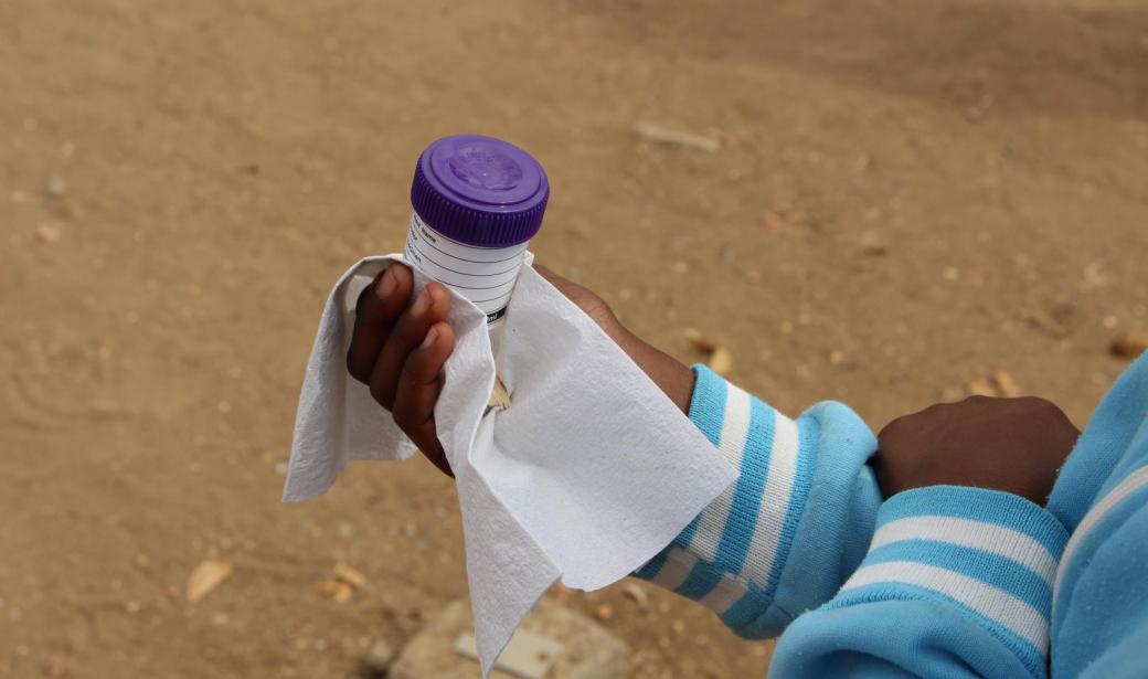 Student at Pantamatenga Primary School in Chobe, holding stool sample container while waiting to use the school bathroom